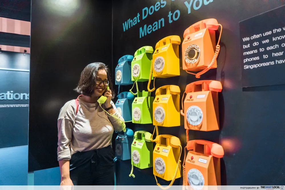 Visitor listening at a wall of colourful rotary phones
