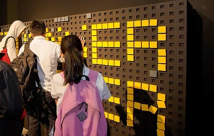 Visitors at a wall of yellow light-up letters